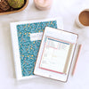 Home Planner blue floral on iPad displaying weekly calendar and printed version in binder on kitchen counter