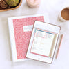 Home Planner pink floral on iPad displaying weekly calendar along with printed version in binder on kitchen counter